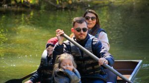 A family of four rowing a canoe on a serene lake during a sunny day, enjoying an outdoor adventure.