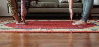 Side view of young ethnic woman stretching body with adorable girl while standing against each other on floor carpet near cozy sofa in modern living room in morning