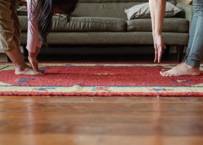 Side view of young ethnic woman stretching body with adorable girl while standing against each other on floor carpet near cozy sofa in modern living room in morning